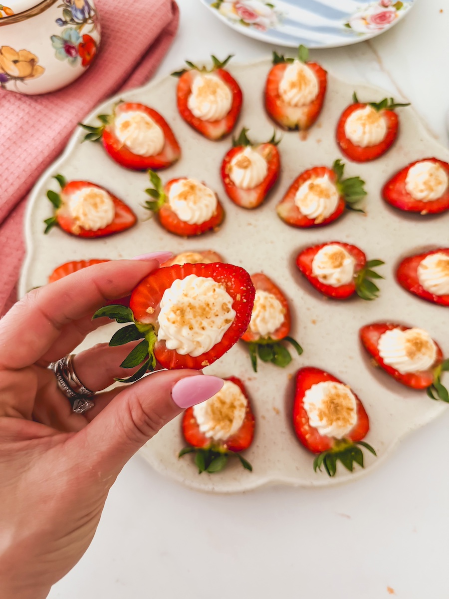 deviled strawberries with cheesecake filling on a tray with a hand holding one
