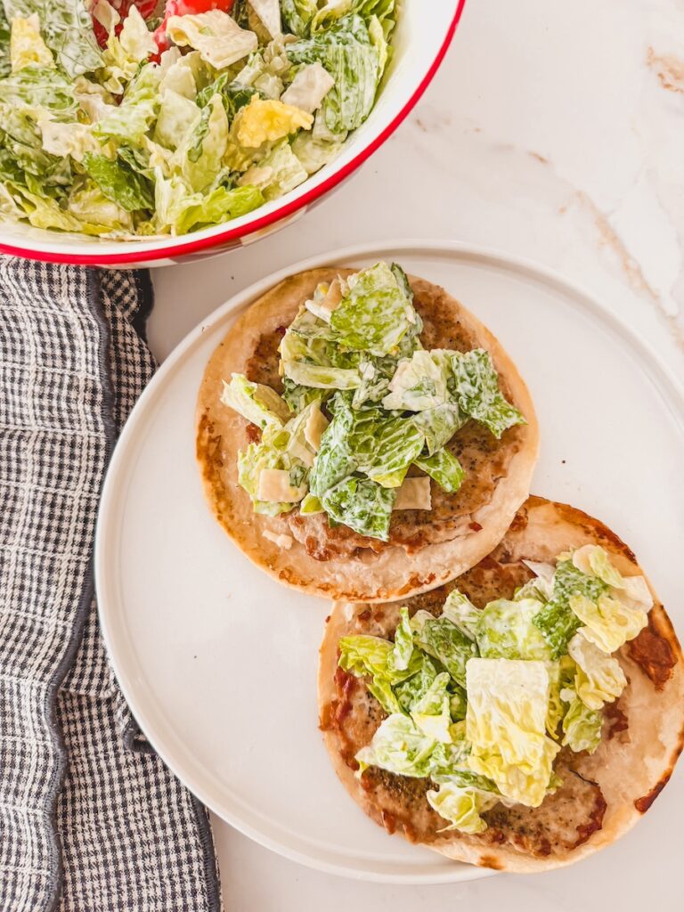 caesar salad on top of ground chicken smashed taco on white plate