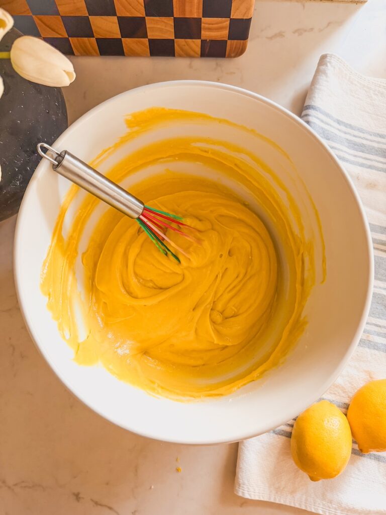 batter in white bowl with whisk in it, and lemons next to bowl