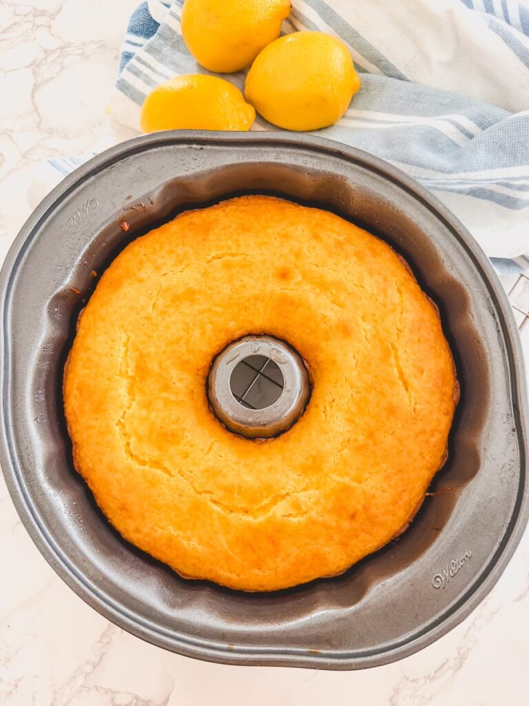baked lemon bundt cake in bundt pan with lemons in background