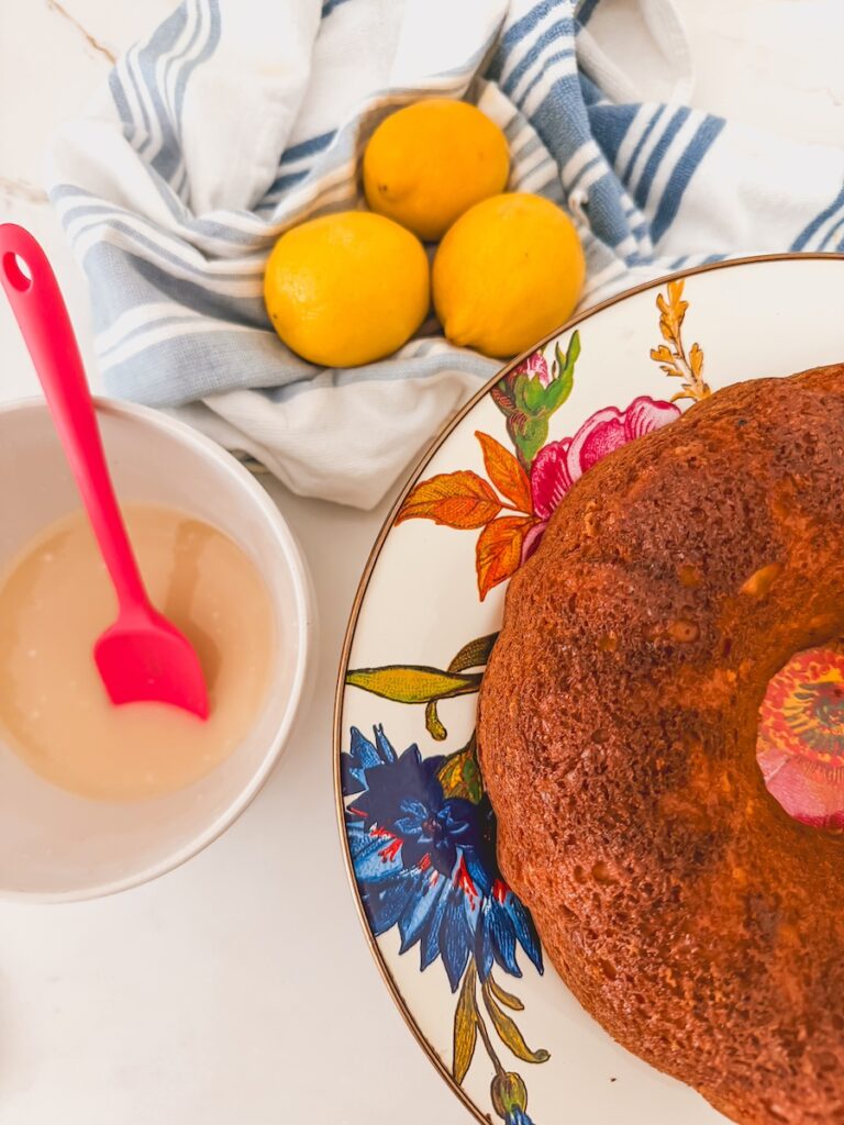 closer shot of baked and unglazed lemon bundt cake with glaze in a bowl next to it and lemons in the background