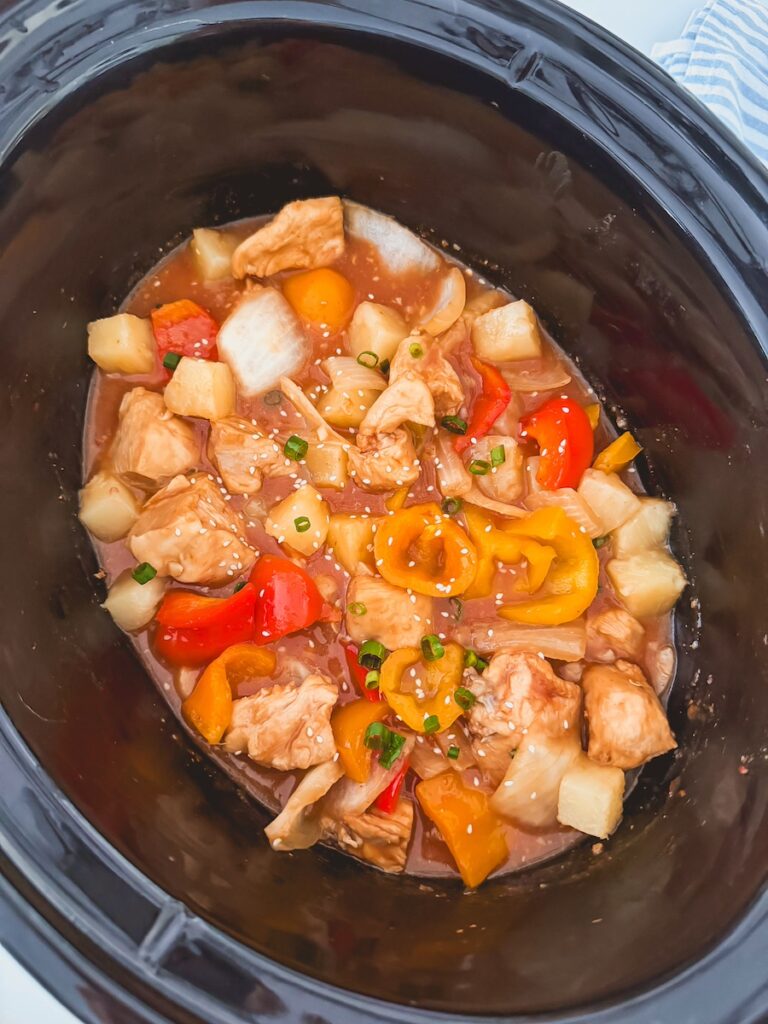 sweet and sour chicken in slow cooker topped with sesame seeds
