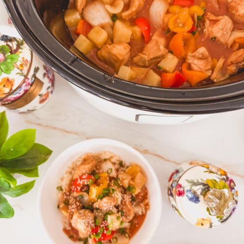 sweet and sour chicken in slow cooker with smaller bowl of sweet and sour chicken topped with sesame seeds next to the slow cooker