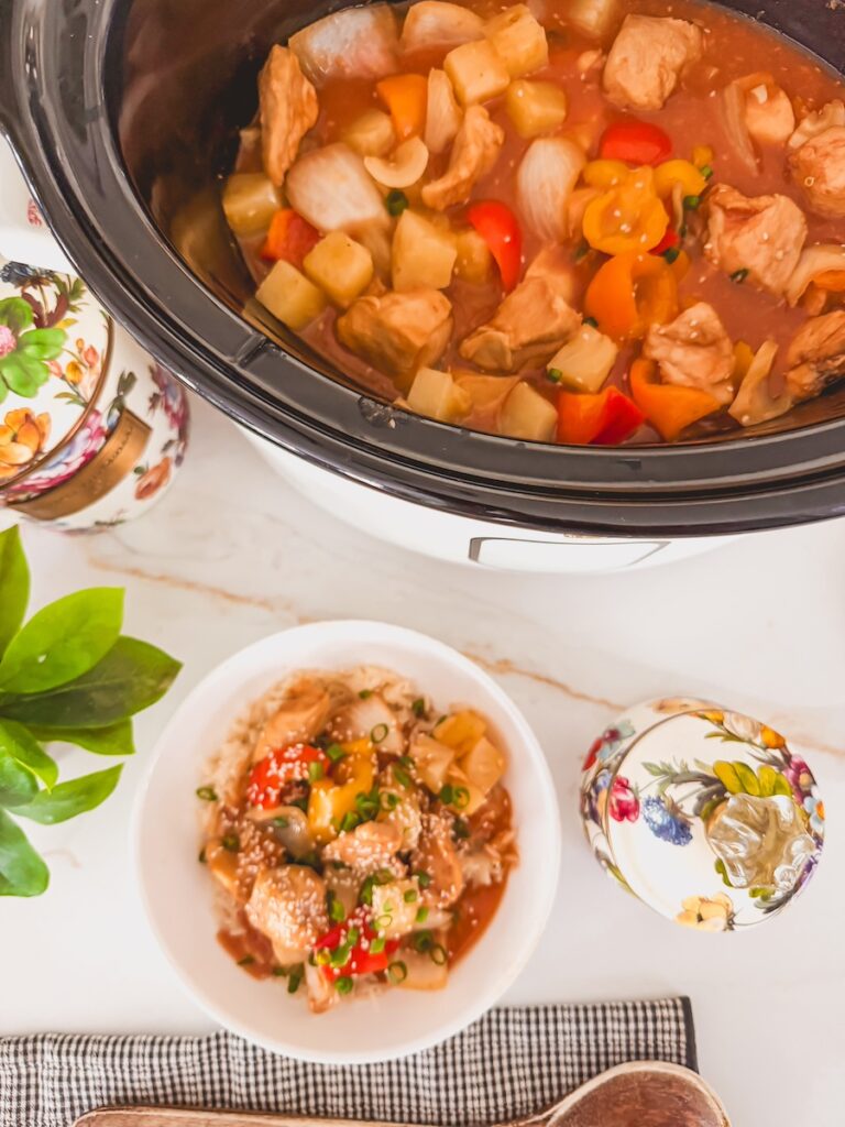 sweet and sour chicken in slow cooker with smaller bowl of sweet and sour chicken topped with sesame seeds next to the slow cooker