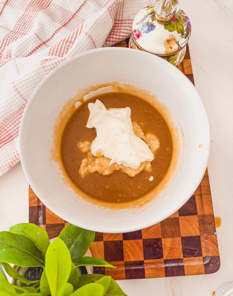 A white bowl with wet ingredients for carrot banana muffins. Greek yogurt is added on top.