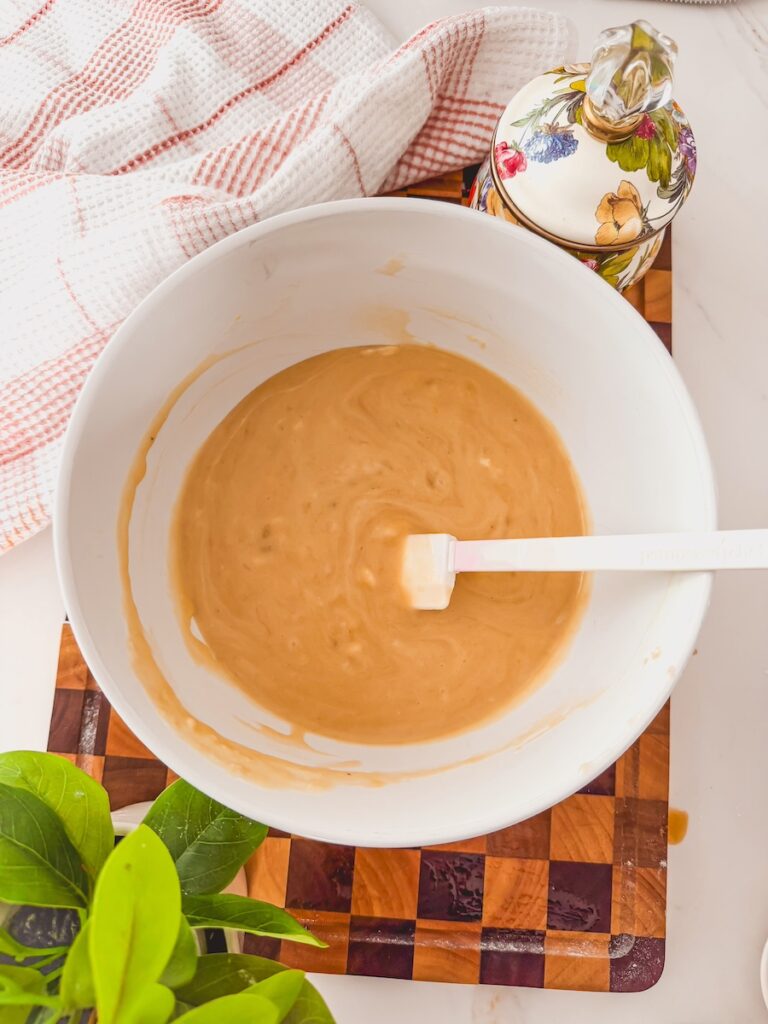 A white bowl with the wet ingredients combined and a white spatula in the center.