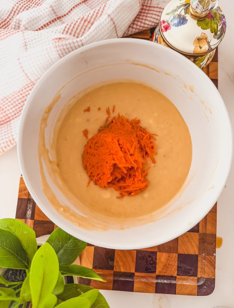 A white bowl with carrot banana muffin batter. Grated carrots are on top.