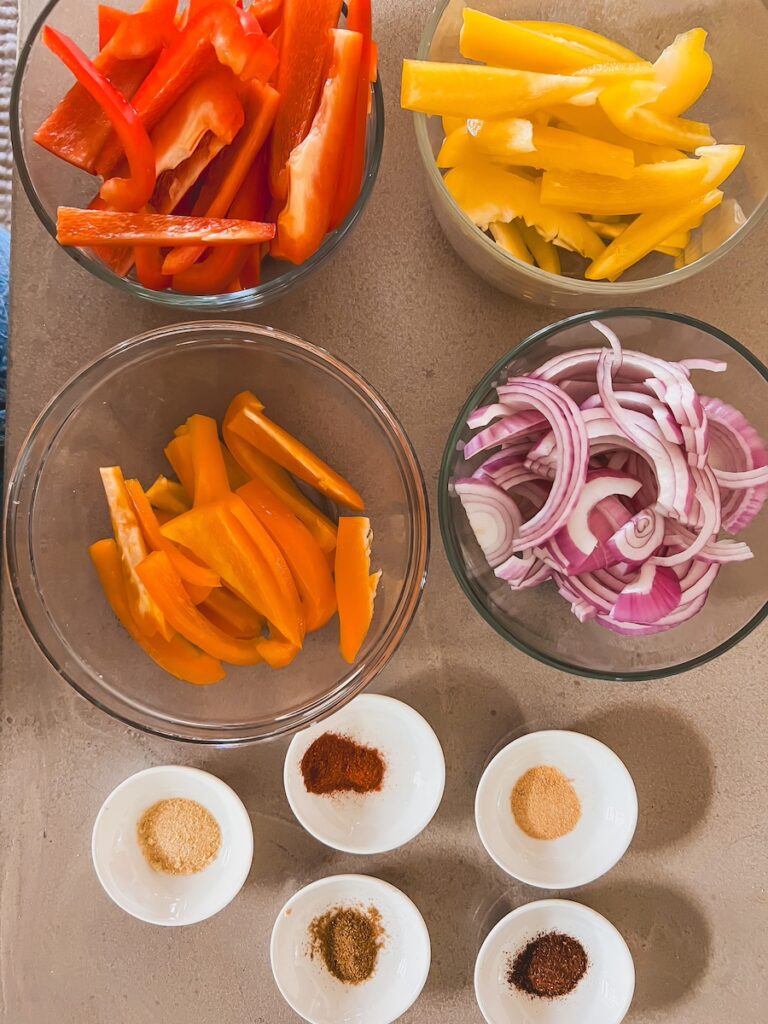 bell peppers and onions in clear bowls. spices in small white bowls.