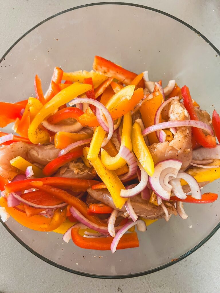 uncooked chicken, bell peppers and onions in clear bowl