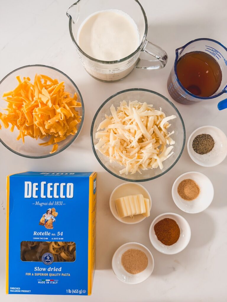 ingredients for one pot creamy cheesy pasta including pasta butter cream broth and shredded cheese in white bowls on white background