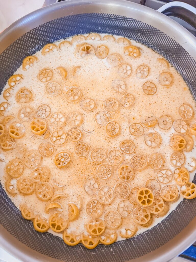 pouring heavy cream and beef broth over pasta in one pot