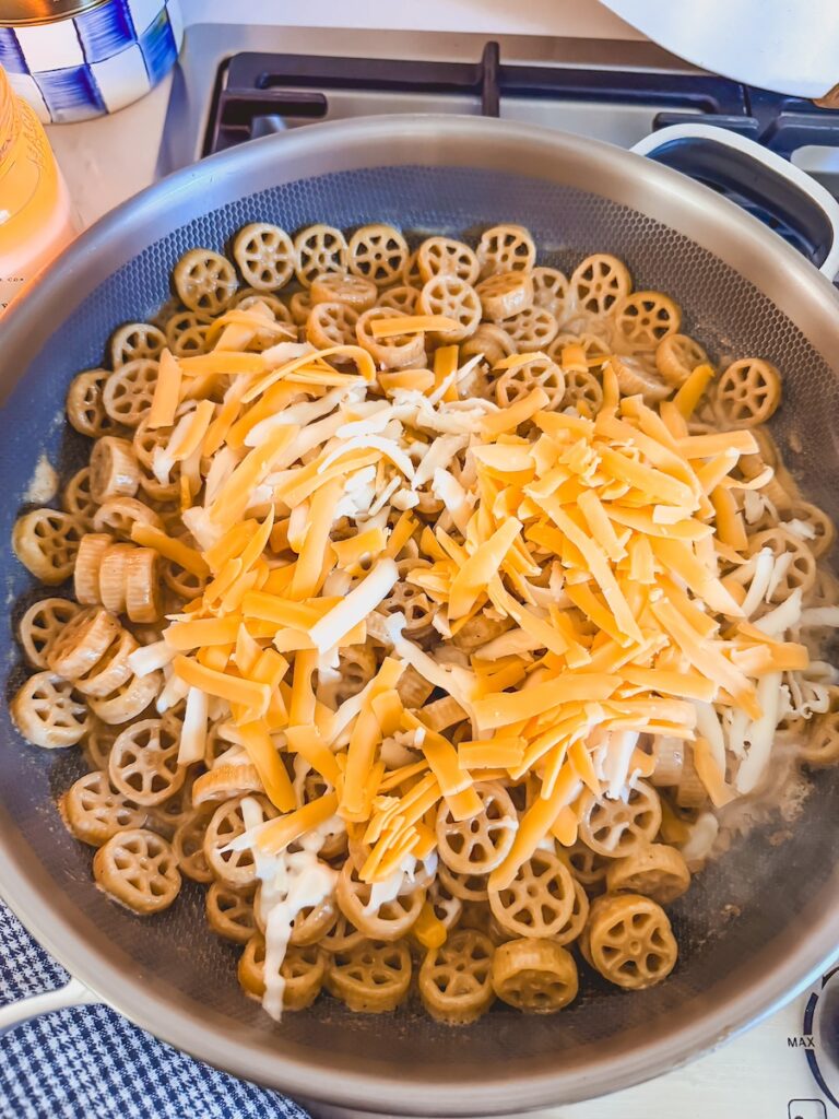 adding cheddar and mozzarella cheese to pasta and stirring until melted