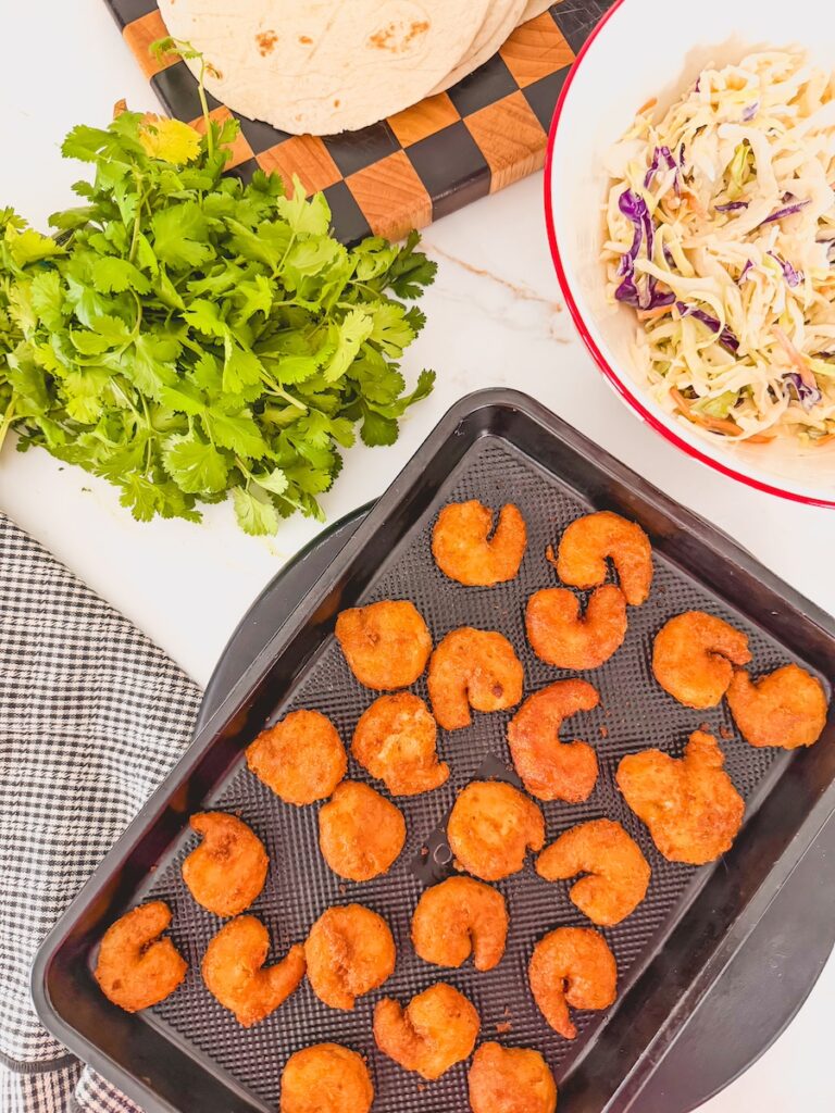 shrimp on baking dish next to bowl of coleslaw and cilantro