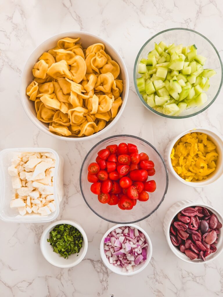 greek tortellini salad ingredients in bowl on marble counter