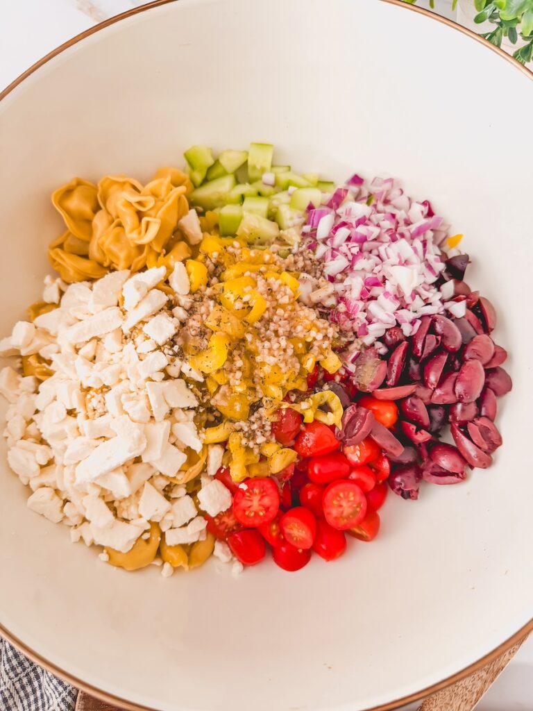 greek tortellini salad components in bowl ready to be mixed