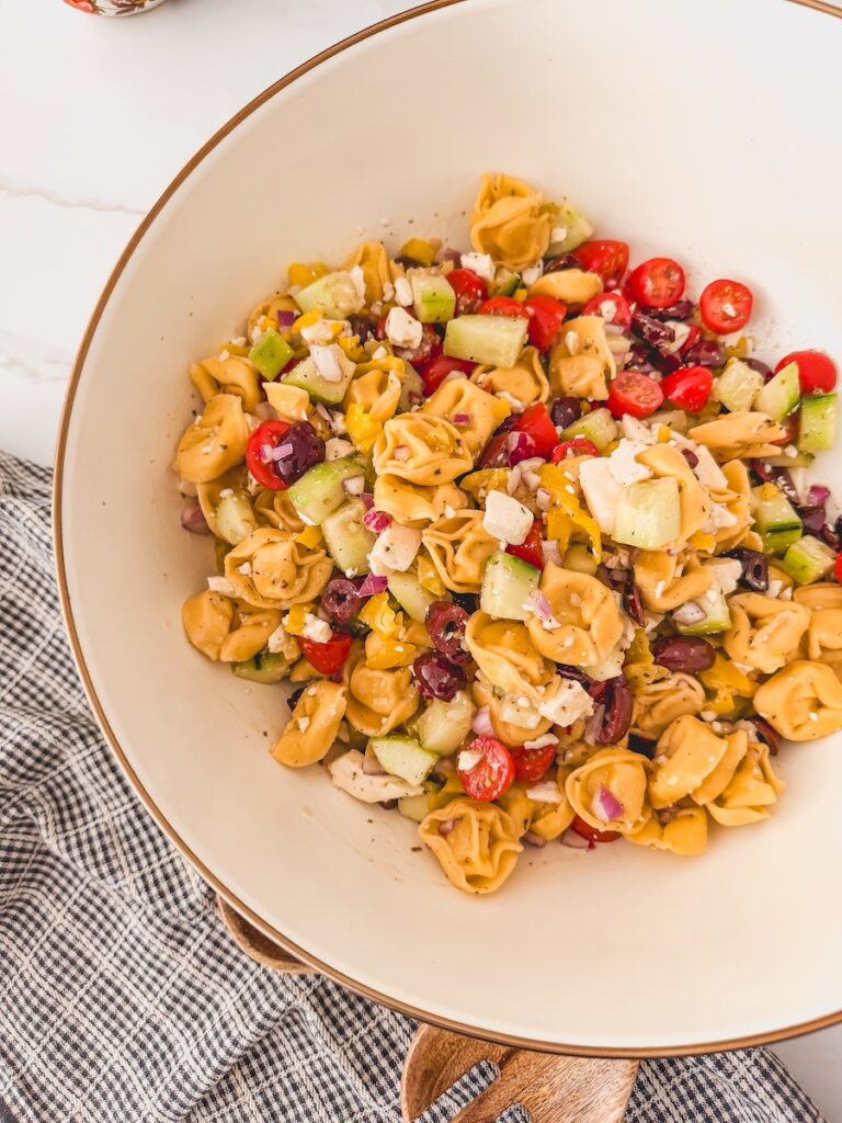 Greek tortellini salad in white bowl, overhead view