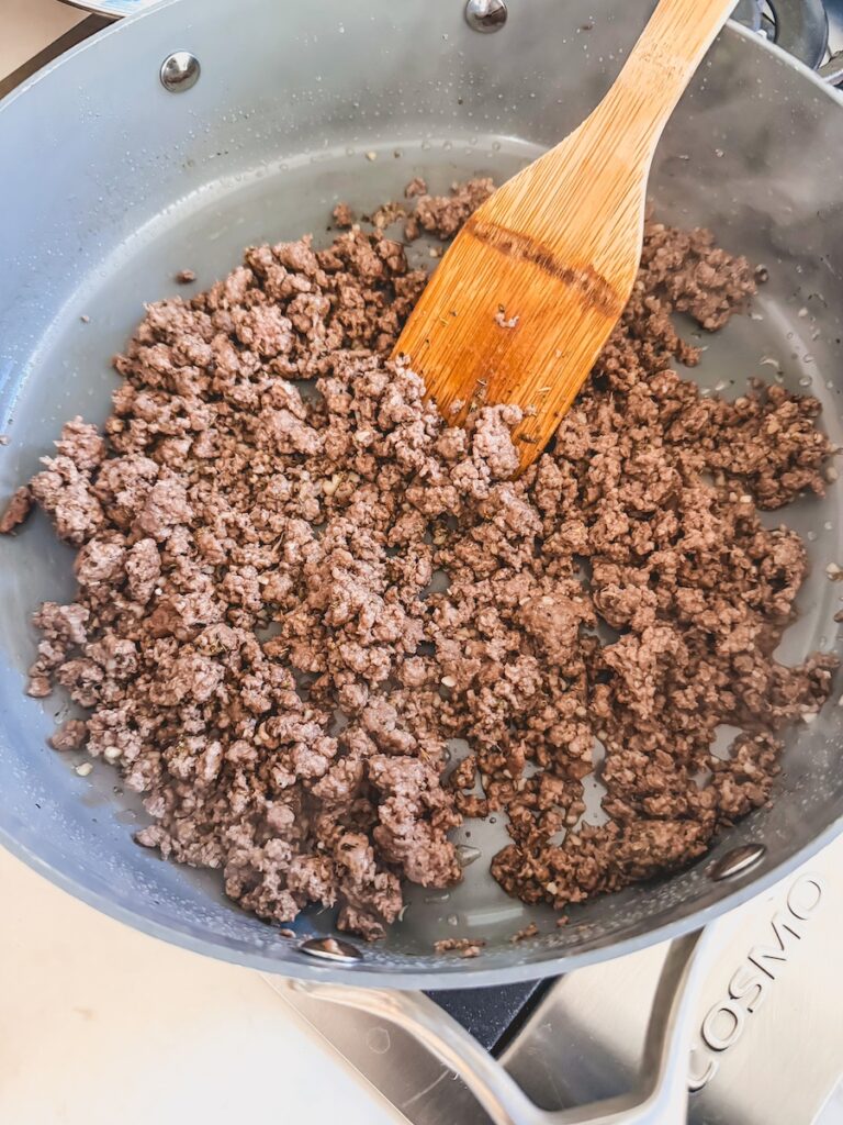 ground beef browning in pan with wooden spoon