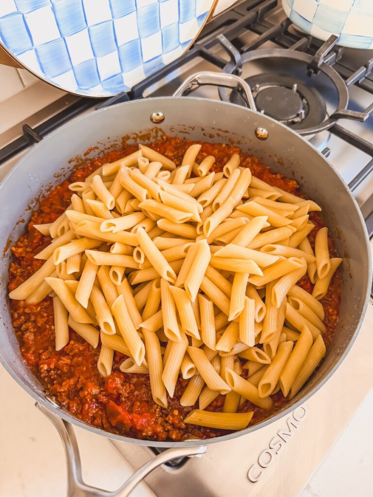 cooked penne pasta added to ground meat-tomato sauce mixture in pan, unmixed