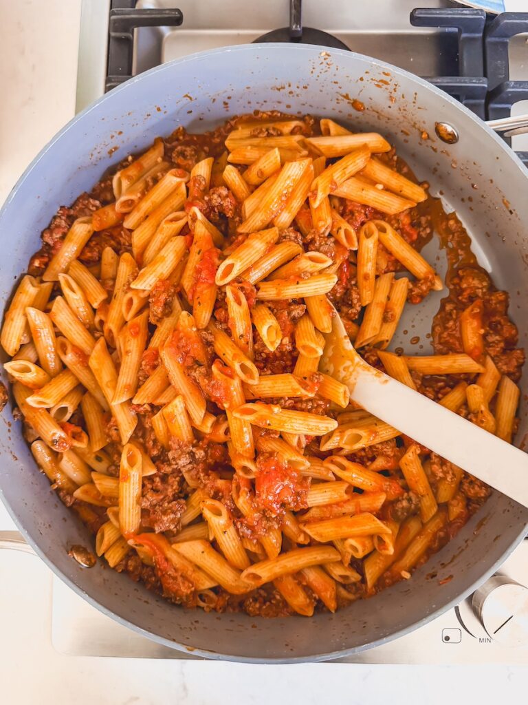 pasta, ground meat, and sauce mixed together in pan with spoon