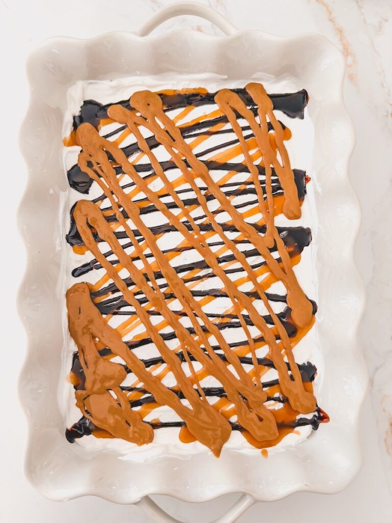 layer of drizzled peanut butter and fudge added to ice cream cake in baking dish
