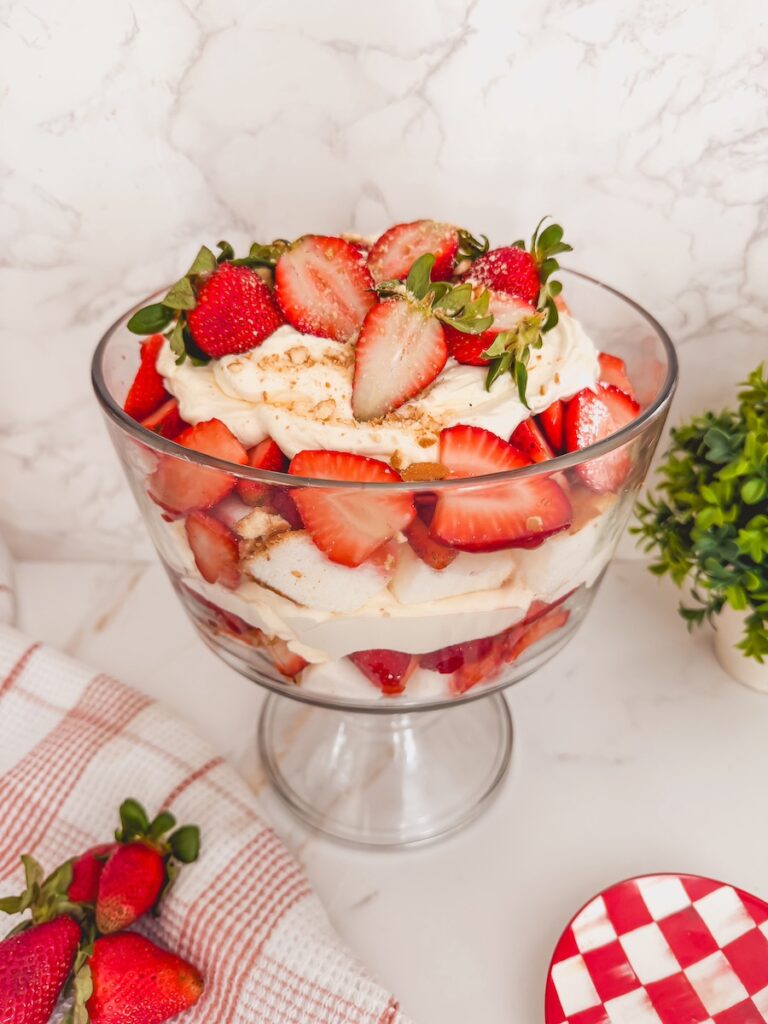 finished assembled strawberry shortcake trifle in glass trifle on counter with strawberries on towel in bottom corner