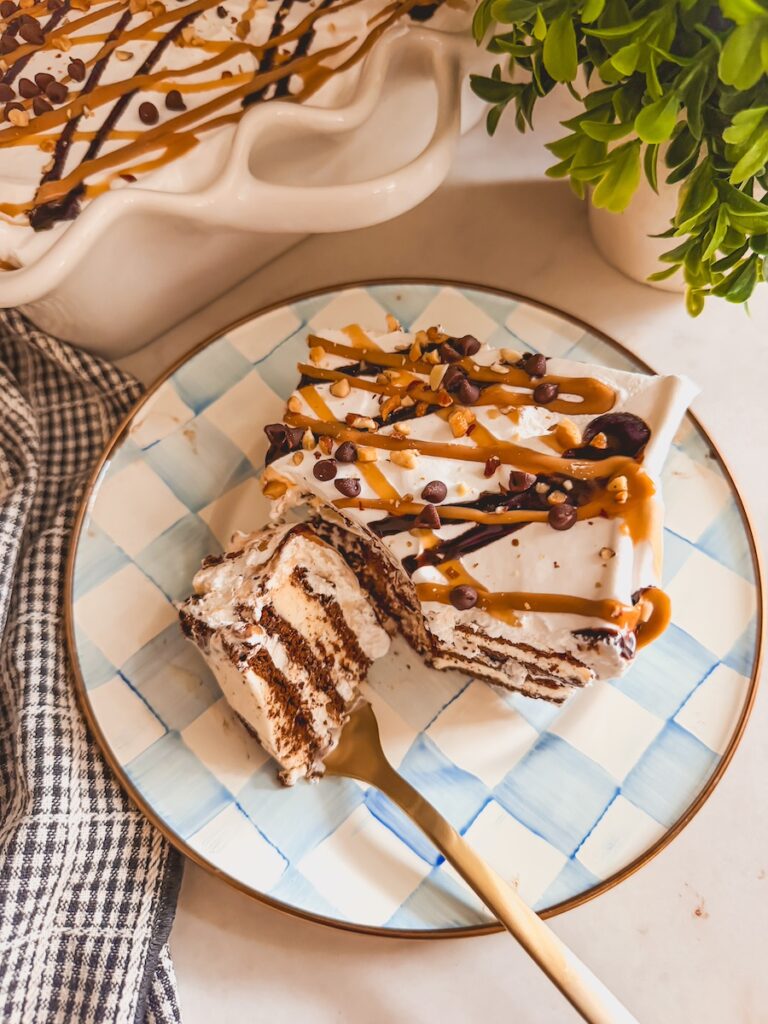 slice of ice cream sandwich cake on plate with a forkful. rest of ice cream sandwich cake in background.