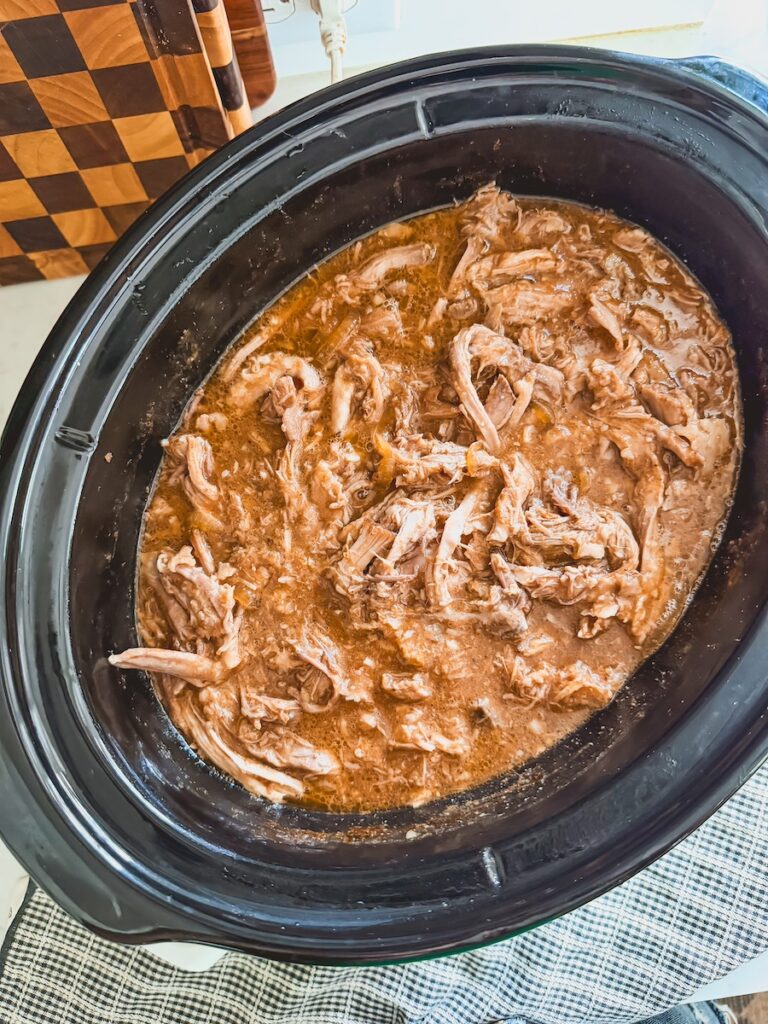 shredded cooked pulled pork in slow cooker mixed with juices