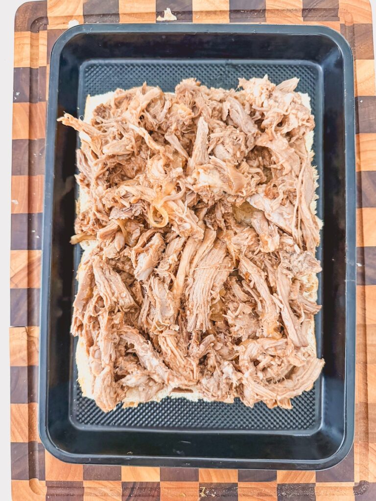 shredded pulled pork layered onto bottom buns, in baking dish