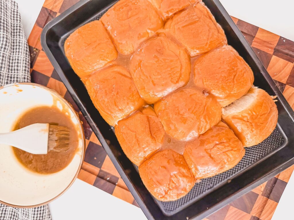 assembled sliders brushed with butter glaze. butter glaze in bowl with brush next to sliders.