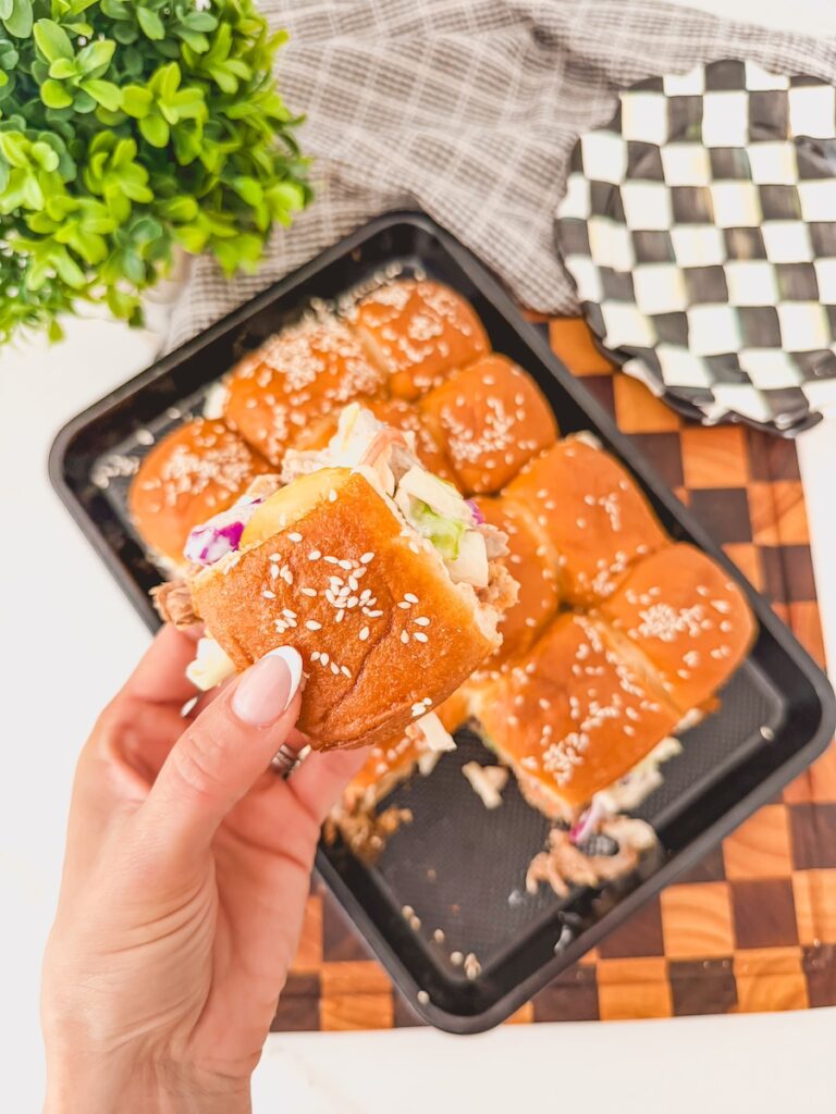 hand holding one removed slider. rest of sliders in tact on baking sheet in background.