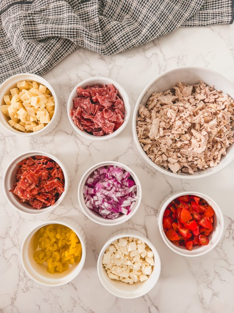 ingredients for Italian grinder chicken salad including chicken, salami, pepperoni, cheese, and banana peppers