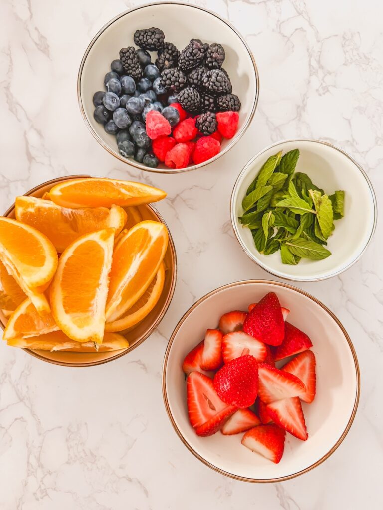 flatlay of bowls of berries, mint, oranges and strawberries