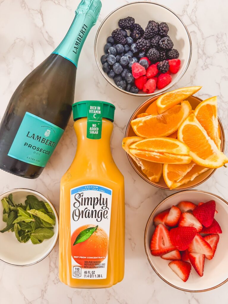 flatlay of ingredients for mimosa drink tower with prosecco, orange juice, fresh berries and oranges