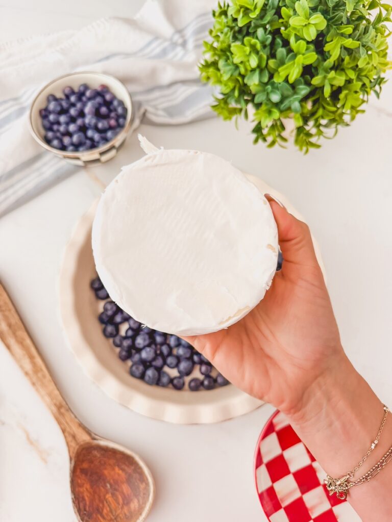 hand holding baked brie with blueberries in the background