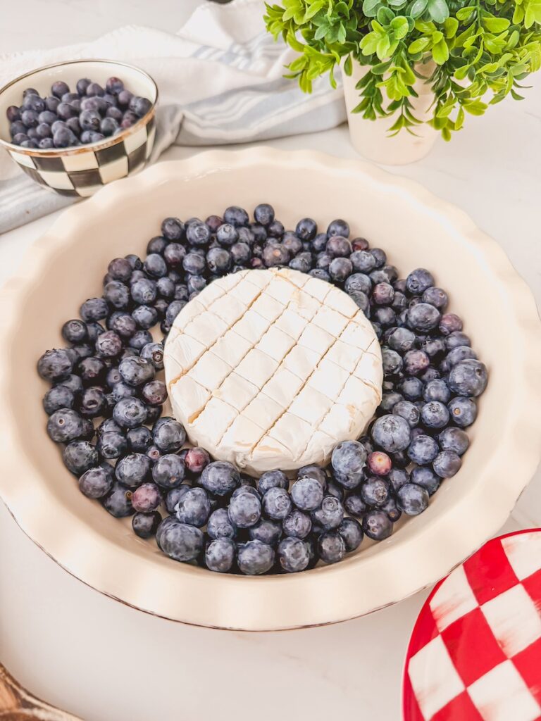 lightly scored baked brie in the middle of a baking dish with blueberries