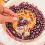 Cracker dipping into baked blueberry brie with gooey melted cheese and honey