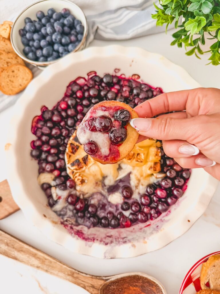 Baked blueberry brie with honey served warm with melted brie cheese, fresh blueberries, and honey drizzle