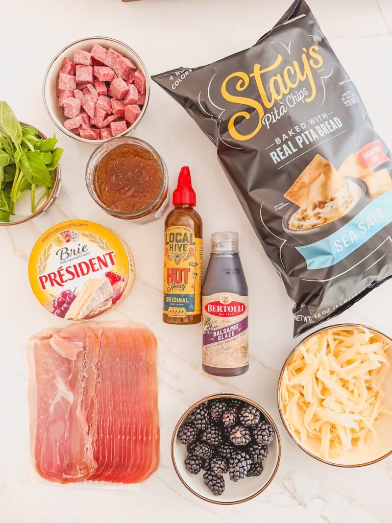 Ingredients for baked charcuterie chips including brie, mozzarella, blackberries, fig jam, prosciutto, salami, and chips