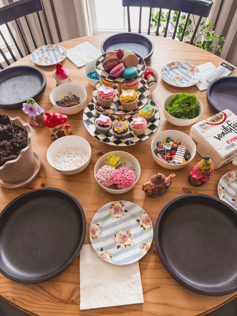 fairy garden table set up with fairy houses, accessories, and cupcakes