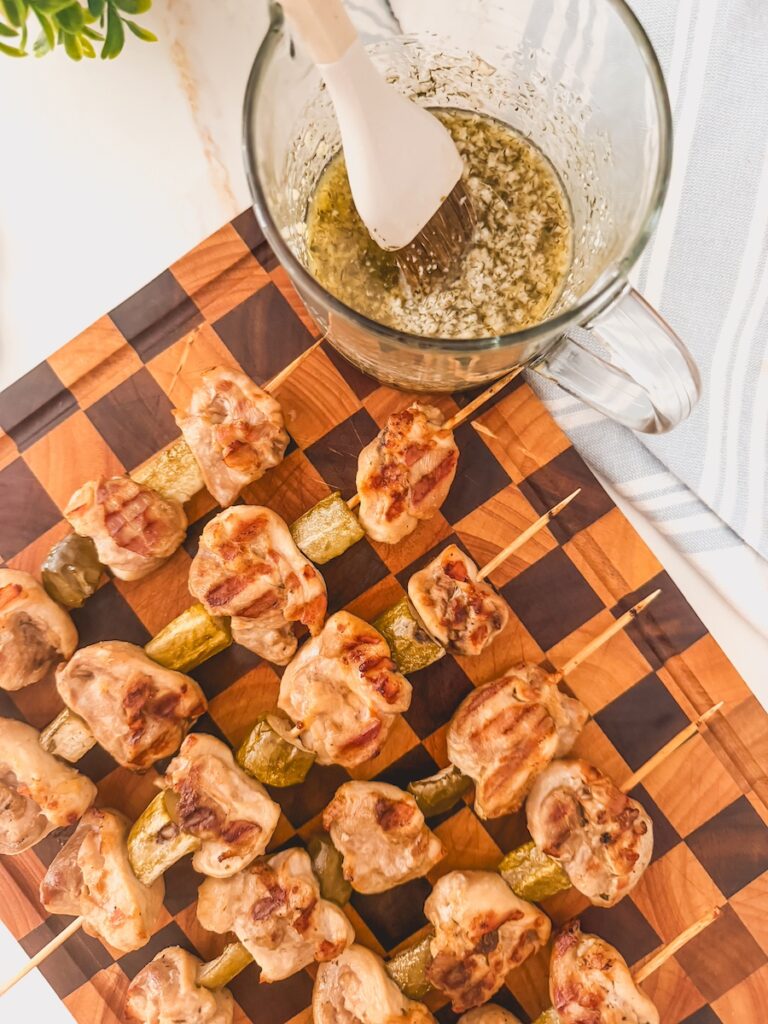 bowl of sauce next to grilled chicken on wood board