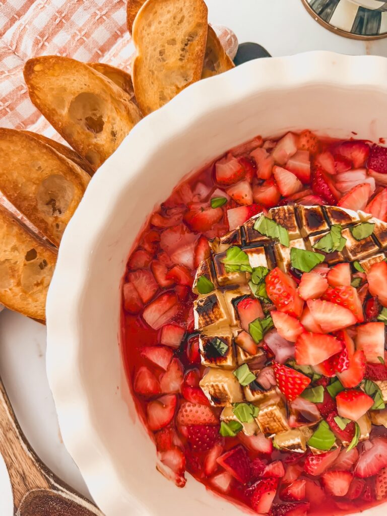 close up of strawberry baked brie in white dish with bread dippers