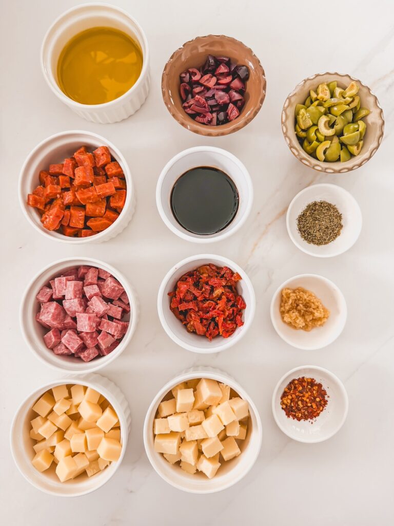 flatlay of ingredients for charcuterie dipping oil such as salami, pepperoni, olives, olive oil, balsamic vinegar, cheeses, garlic, and spices