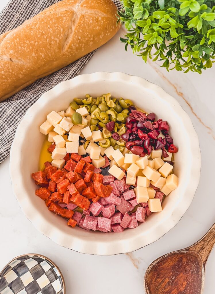 charcuterie ingredients added to bowl with salami, pepperoni, olives, sun dried tomatoes, cheeses