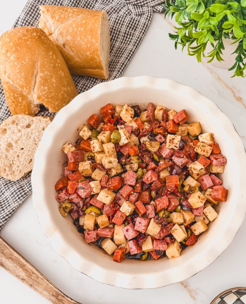 charcuterie dip full of salami, pepperoni, olives, cheeses and oil in white bowl with bread