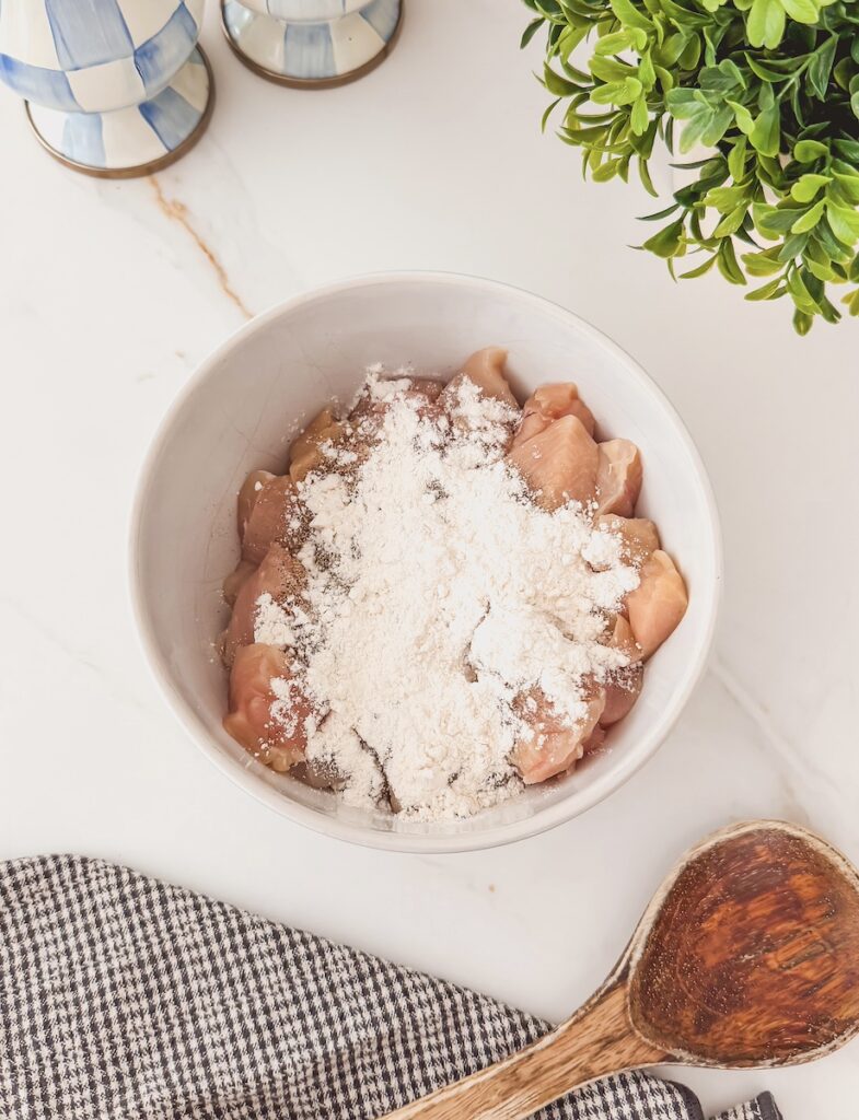 Chicken cubes with flour over top in a white bowl.
