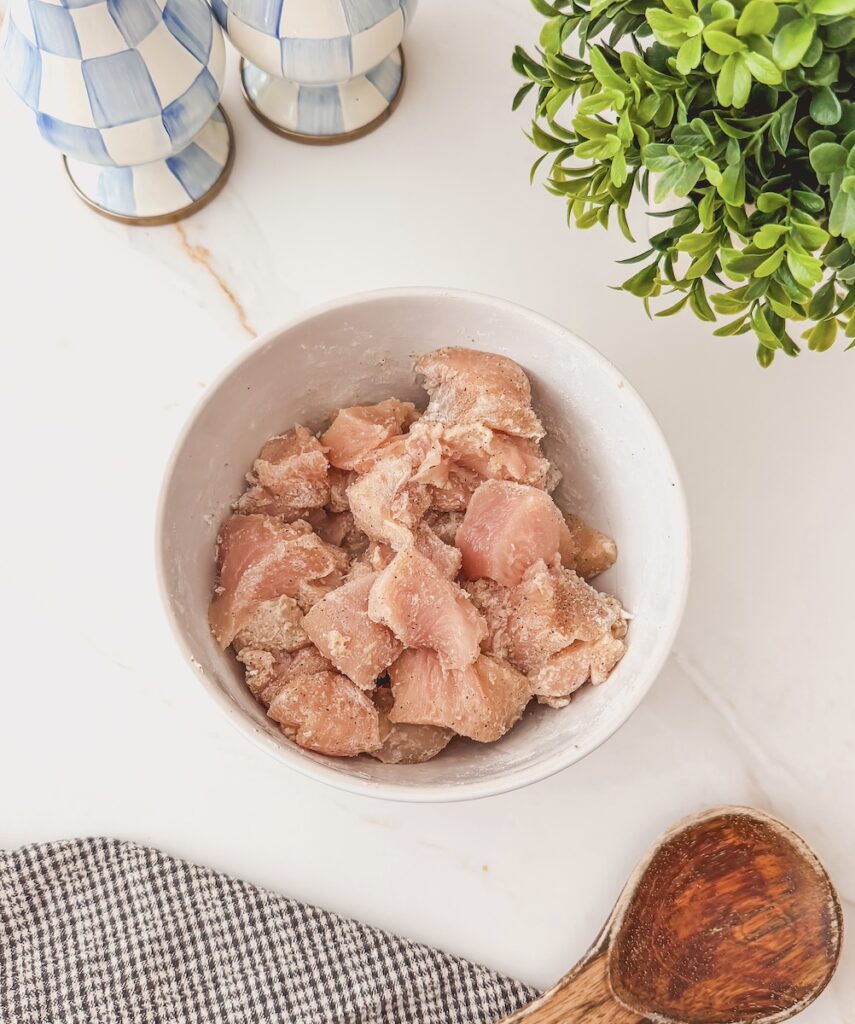 Chicken cubes tossed in flour in a white bowl.