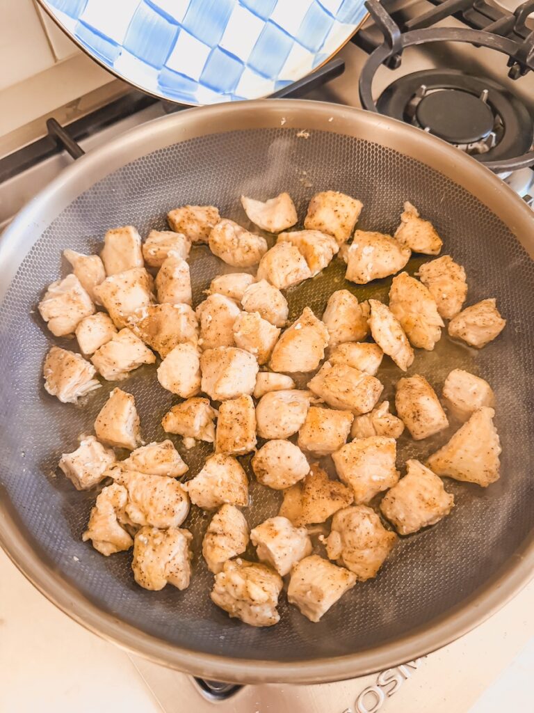 Cooked chicken cubes in a large nonstick pan.