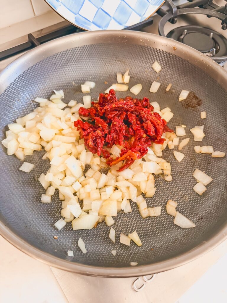 A skillet with onions and sundried tomatoes.