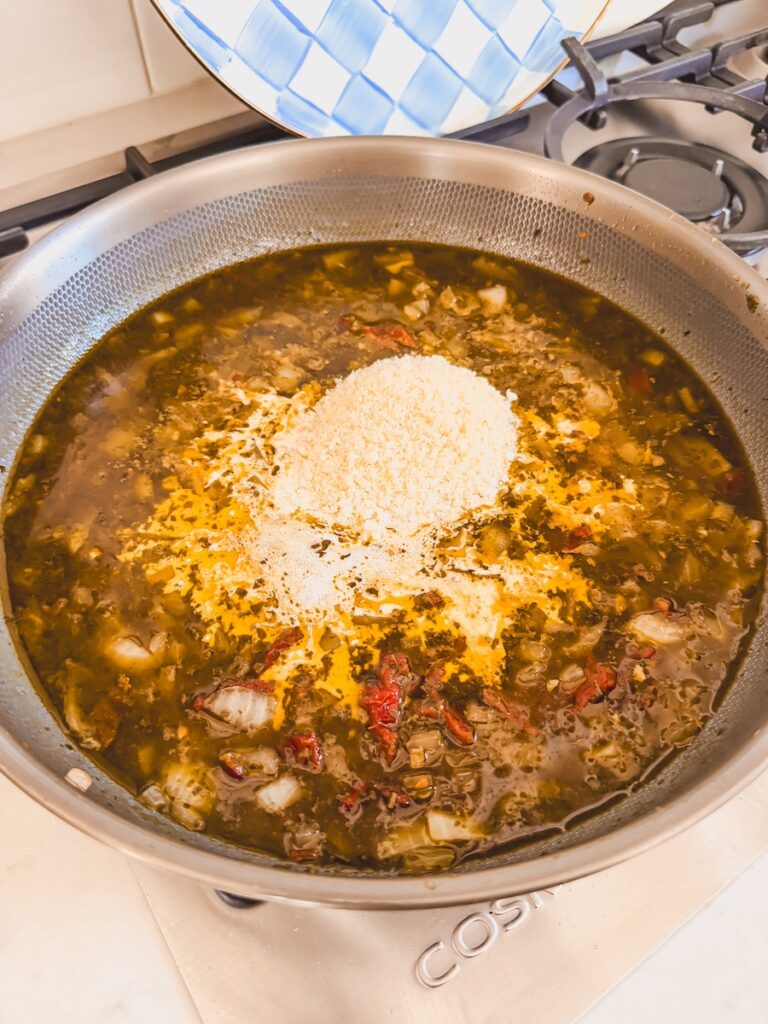 A skillet with broth, onions, sundried tomatoes, and parmesan cheese.
