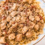 Close up image of chicken pesto pasta in a blue and white checkered bowl.